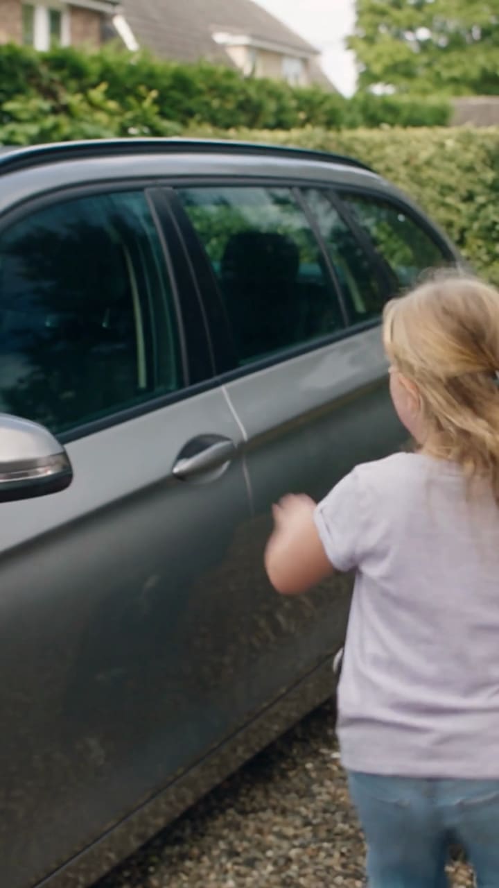 A child washes the car in the driveway.