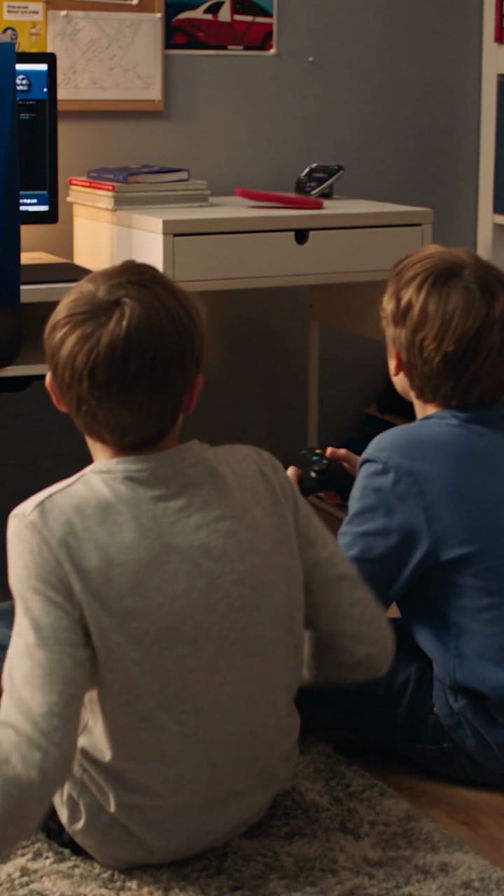 Two boys sit in front of the television playing with controllers.